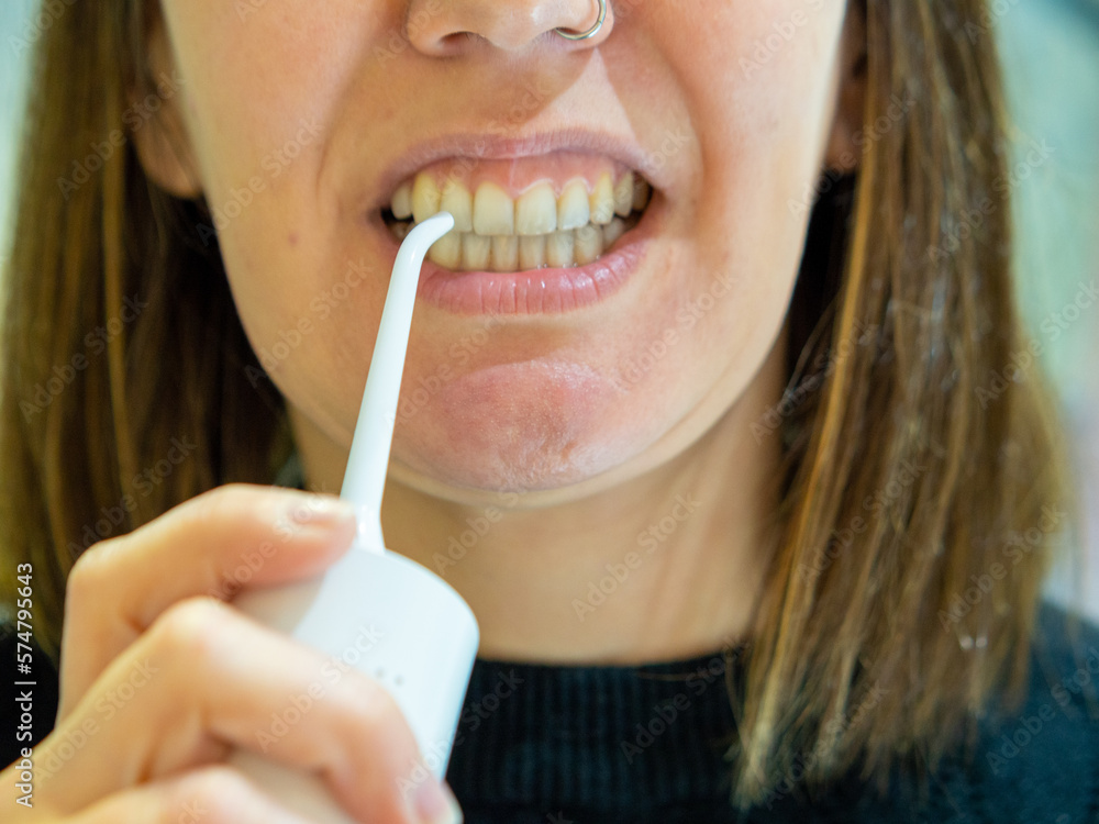 Naklejka premium Healthy Oral Hygiene: Young woman Using domestic dental water flosser 