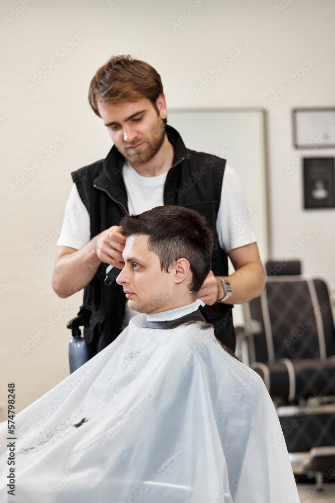 Fototapeta premium Barber shaving caucasian man in barber shop.