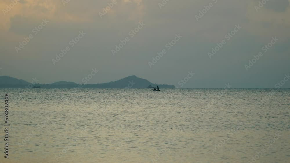 In the evening sea, the silhouette of lonely fishermen on a boat is visible on the horizon In the evening sea, the silhouette of lonely fishermen on a boat is visible on the horizon