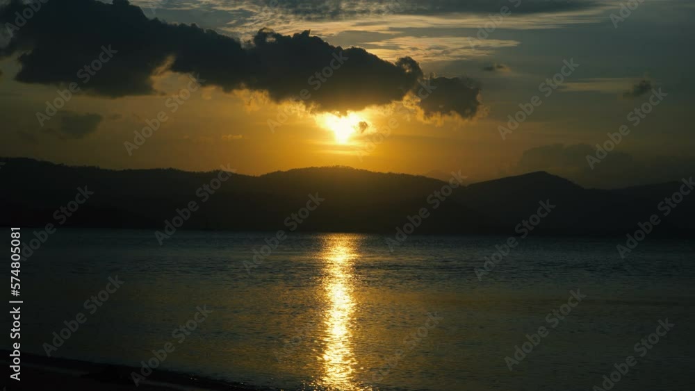 The sun sets behind the mountain, reflecting in the sea The sun sets behind the mountain, reflecting in the sea