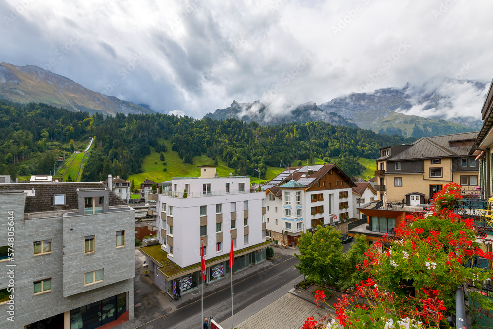 View from a hotel balcony with flowers of the Swiss town of Engelberg, Switzerland, and the scenic Mt Titlis mountain shrouded in clouds and fog.