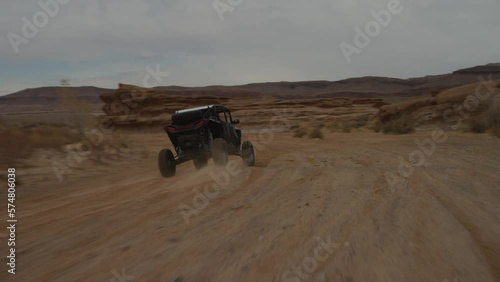 Tracking shot chasing behind UTV driving fast in red sandy wash in Utah desert photo
