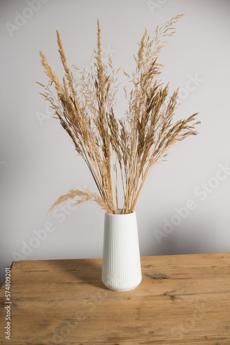 Dried flowers in a white vase stand on a wooden table