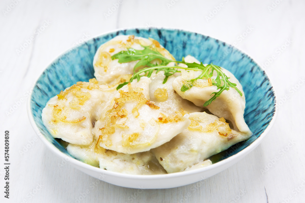 Pierogi or Varenyky ( dumplings ) stuffed dumplings sprinkled with fried onions and butter with herbs in a plate isolated on a wooden table. Ukrainian or Polish traditional dish. Pierogi or Varenyky ( dumplings ) stuffed dumplings sprinkled with fried onions and butter with herbs in a plate isolated on a wooden table. Ukrainian or Polish traditional dish.