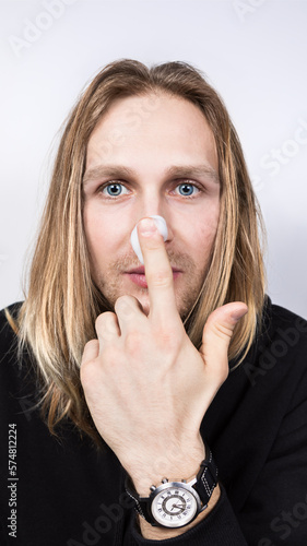 A real young handsome long haired blond with blue eyes and applying cleansing foam on his nose with the finger of one hand.Cosmetology for men,professional and home skin and hair care