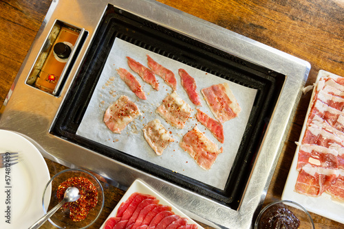 Slices of beef meat being grilled korean style on grill with sauce and seasoning on the side