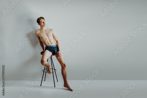 skinny and scrawny boy is rawboned and underweight but show proud and confident his body positivity and slim shape while sit on barstool and have self-esteem and self love for his anatomy photo