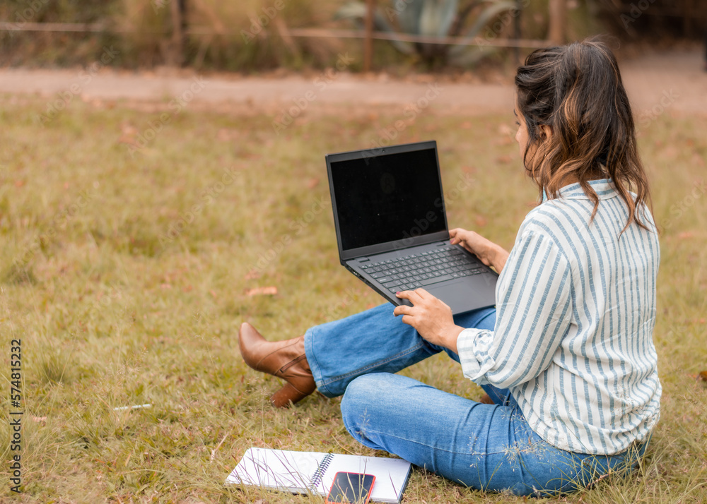 woman from behind sitting on the grass working on her laptop woman from behind sitting on the grass working on her laptop
