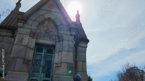 footage of a stone mausoleum with a metal door, two pillars and the word Austell on top surrounded by lush green trees, plants and headstones at the Oakland Cemetery in Atlanta Georgia USA photo