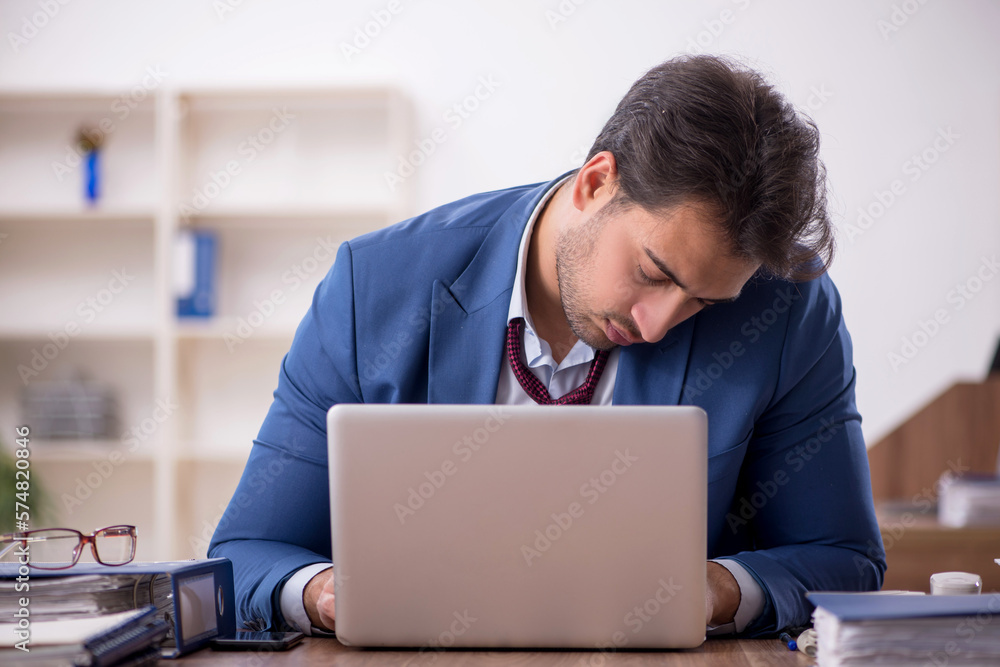 Young male employee unhappy with excessive work in the office Young male employee unhappy with excessive work in the office