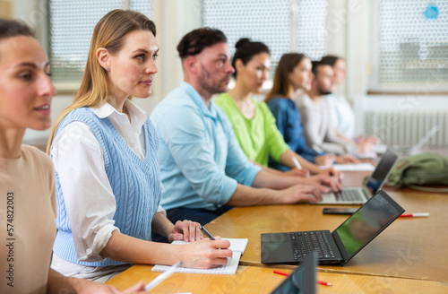 Group of young students searches for information on a laptop and writes it down in a copybooks, studying in a university ..auditorium during classes