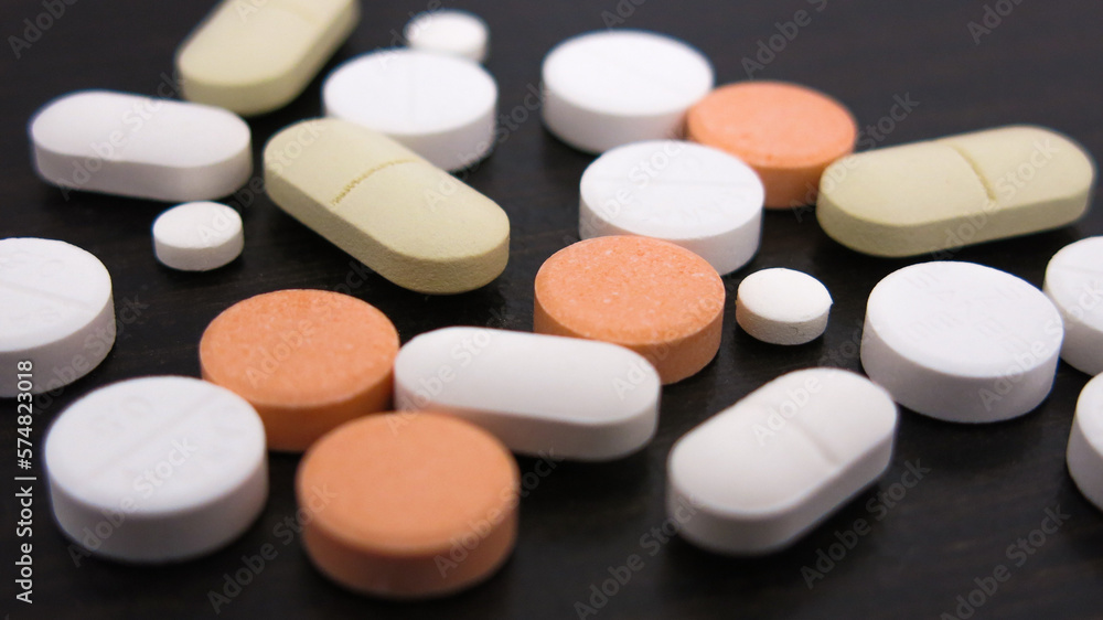 Assorted scattered pharmaceutical medicine pills and tablets in various colour and size isolated in wooden black background Assorted scattered pharmaceutical medicine pills and tablets in various colour and size isolated in wooden black background