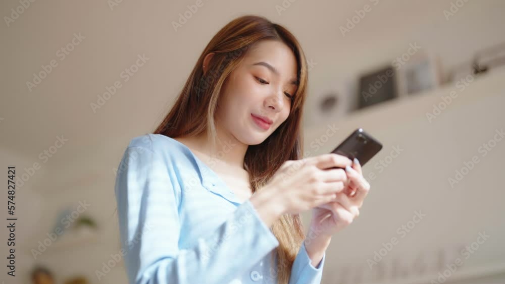 Happy young asian woman relax on comfortable couch at home texting messaging on smartphone, smiling girl use cellphone chatting, browse wireless internet on gadget, shopping online from home Happy young asian woman relax on comfortable couch at home texting messaging on smartphone, smiling girl use cellphone chatting, browse wireless internet on gadget, shopping online from home