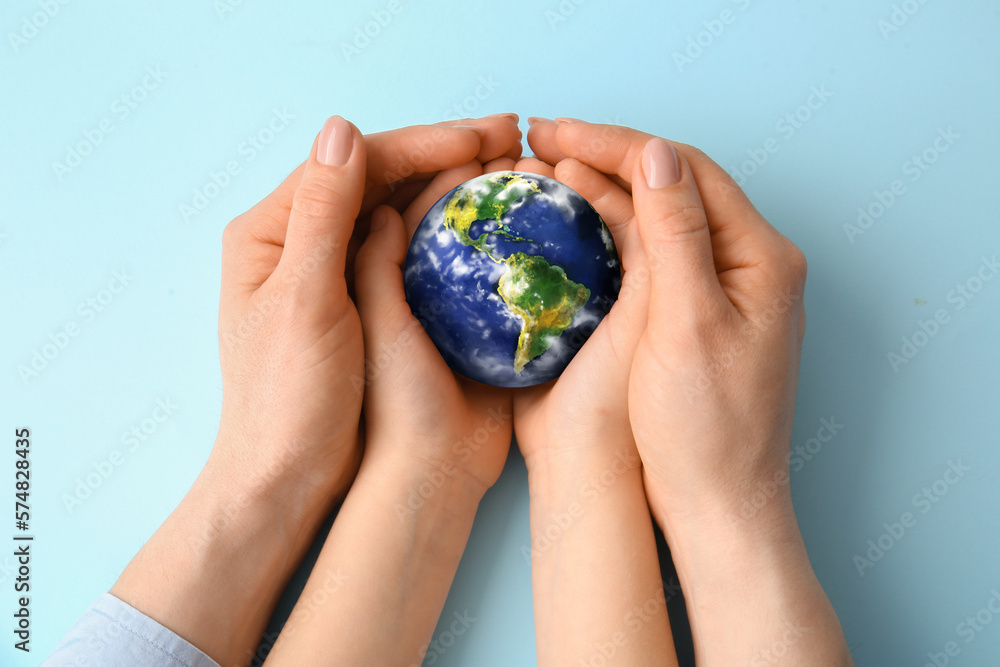 Hands of mother and child holding small planet Earth on light blue background Hands of mother and child holding small planet Earth on light blue background