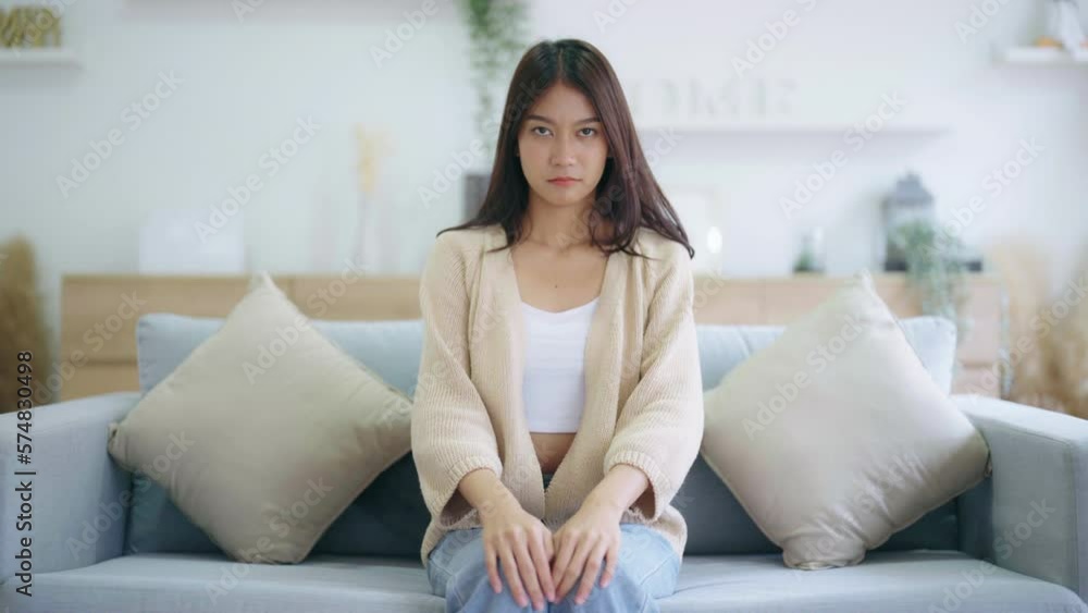 Unhappy teen asian girl bad face and hand thumb down with sitting on couch at home. She thumb down meaning feeling bad Unhappy teen asian girl bad face and hand thumb down with sitting on couch at home. She thumb down meaning feeling bad
