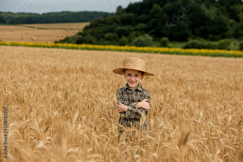 Portrait of smiling little farmer boy in a plaid shirt and straw hat in a wheat field.