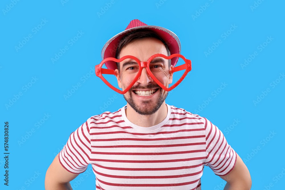 Funny young man in eyeglasses on blue background, closeup. April Fools' Day celebration Funny young man in eyeglasses on blue background, closeup. April Fools' Day celebration