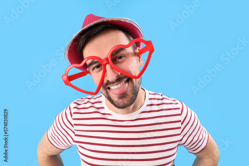 Funny young man in eyeglasses on blue background, closeup. April Fools' Day celebration