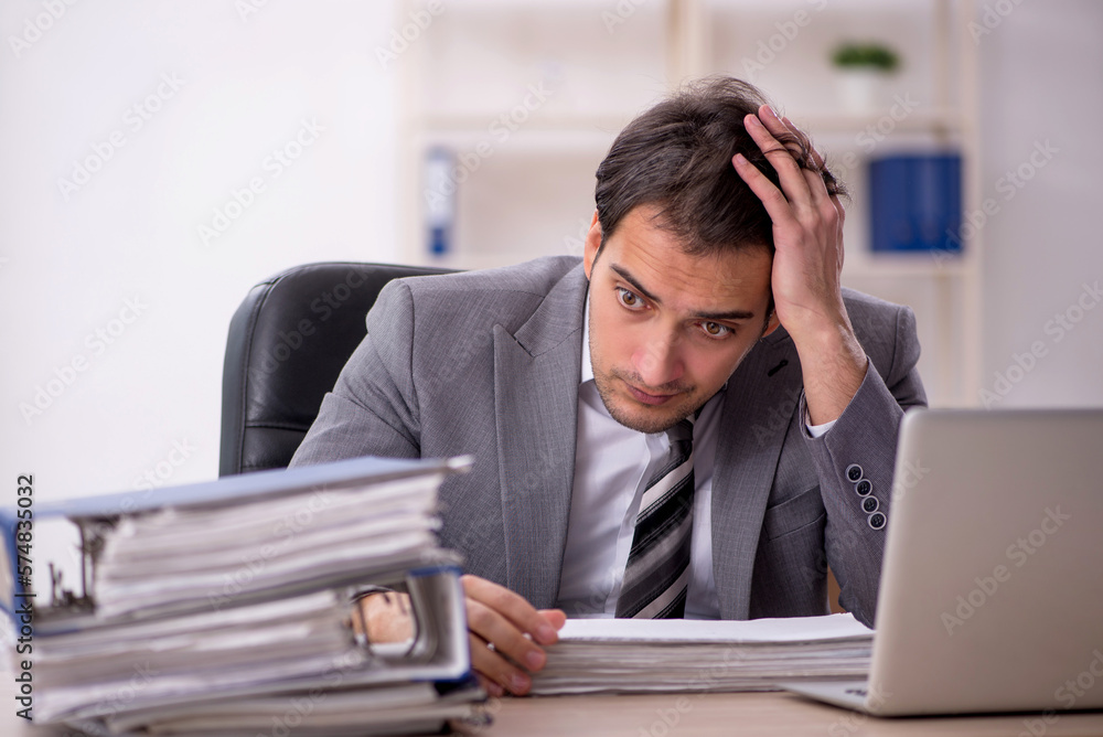 Young male employee unhappy with excessive work in the office Young male employee unhappy with excessive work in the office