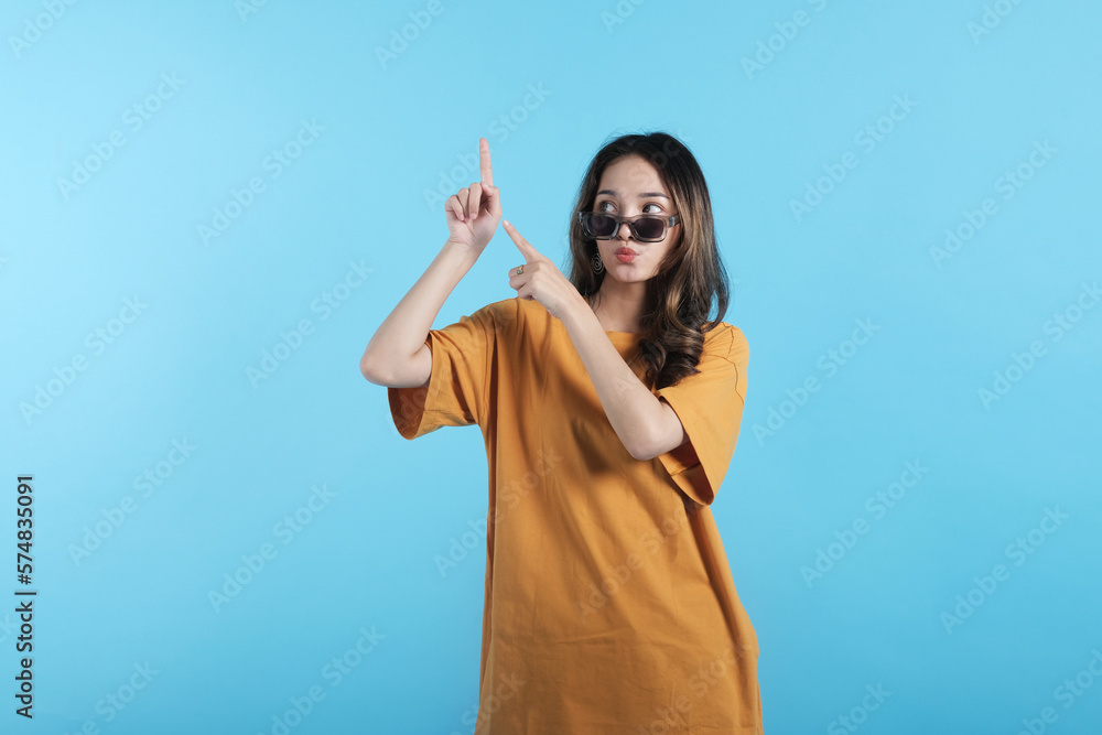 Asian young female using a sunglasses, gesture with her hands pointing to empty space on blue background Asian young female using a sunglasses, gesture with her hands pointing to empty space on blue background
