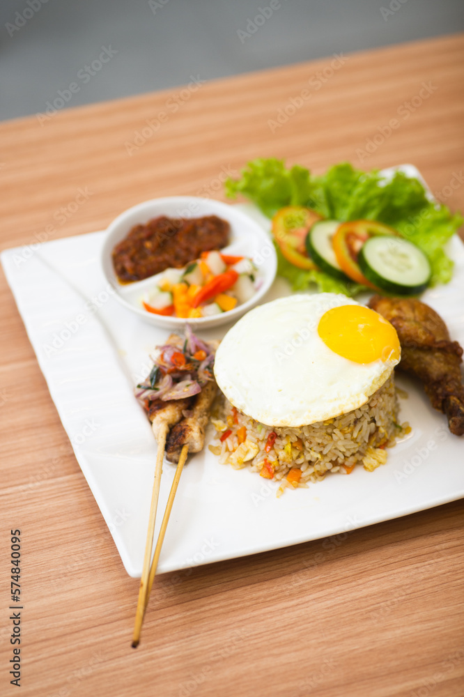 Indonesian fried rice served with a side of drumstick and satay, topped with sunny side egg Indonesian fried rice served with a side of drumstick and satay, topped with sunny side egg
