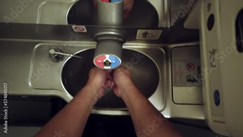 Pov handwash on flight with view of faucet and sink with taps or push button to dispense water for washing hand with trash in lavatory on board in airplane