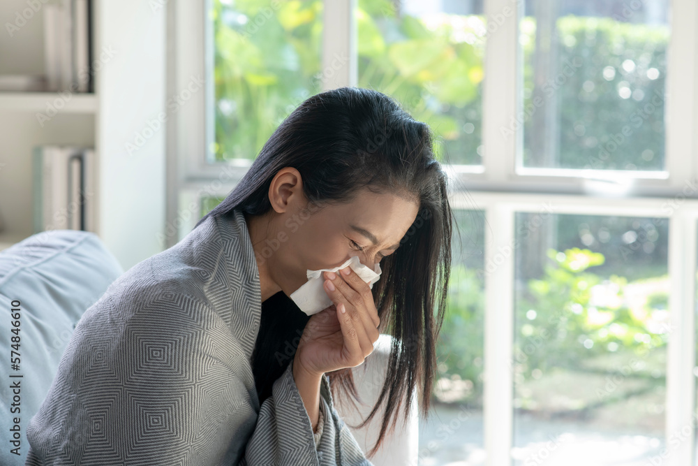 Ill young Asian woman covered with blanket blowing running nose got