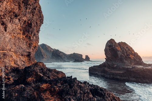 A picturesque view of rock formations in the ocean, bathed in the warm light of the setting sun. (ID: 574847851)