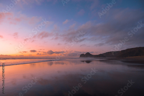 A stunning view of Bethells Beach, captured at sunset, with vibrant tones of pink, violet, and orange filling the sky. photo