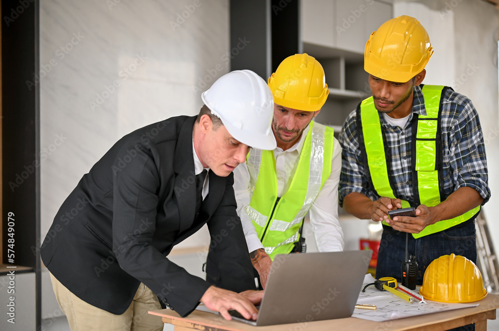 Caucasian businessman using laptop while meeting with a team of construction engineers Caucasian businessman using laptop while meeting with a team of construction engineers