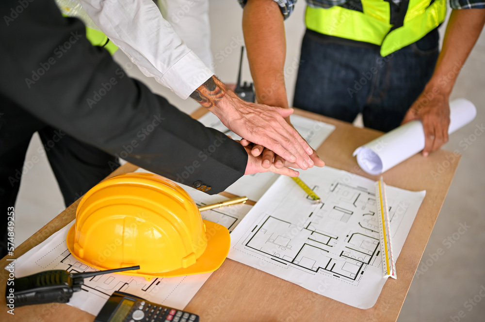 Cropped image of a team of construction workers and a businessman putting their hands together Cropped image of a team of construction workers and a businessman putting their hands together