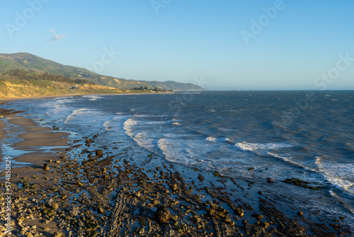 Golden hour views of Carpinteria State Beach on the California rocky coastline. Tall grasses blowing in the wind, dirt paths, rusty railroad tracks, bluffs, large eucalyptus trees, breaking waves. © Adam