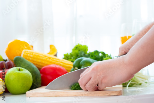 Hands using a knife chopping vegetable over wooden carving board on the table at white curtain background