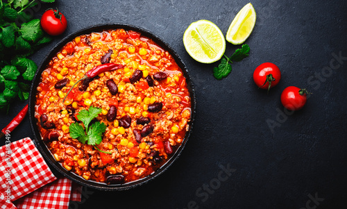 Chili con carne with beef, red beans, paprika, corn and hot peppers in tomato sauce, spicy tex-mex dish in a cooking pot, black table background, top view