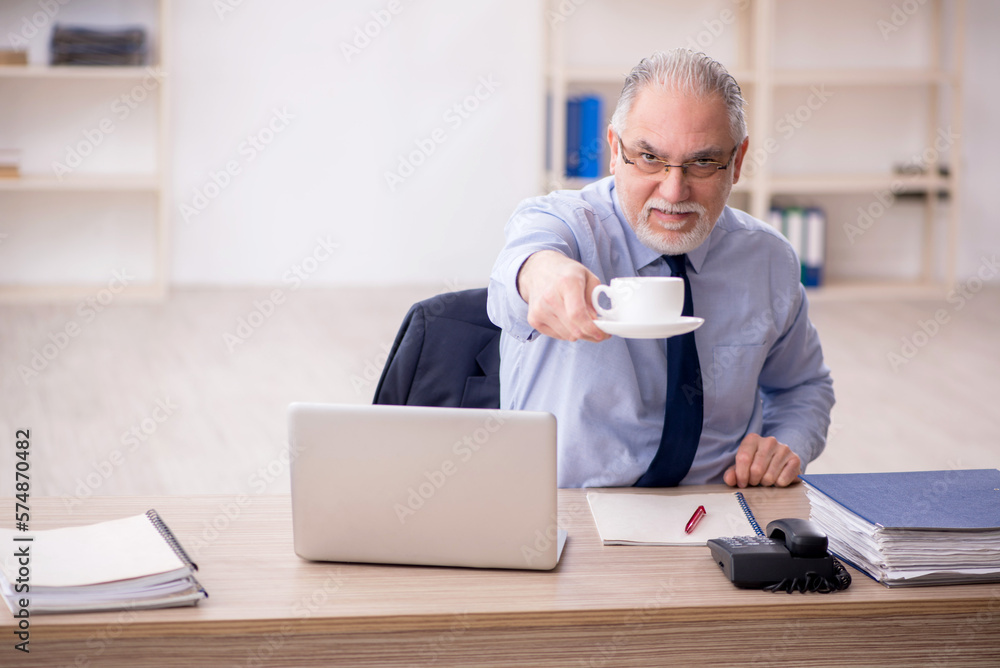 Old male employee drinking tea in the office