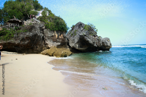 Photo of a beach scene with large rocks, sand and a cloudless blue sky