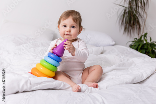 adorable baby in white shirt playing with colorful toy on bed, banner, card