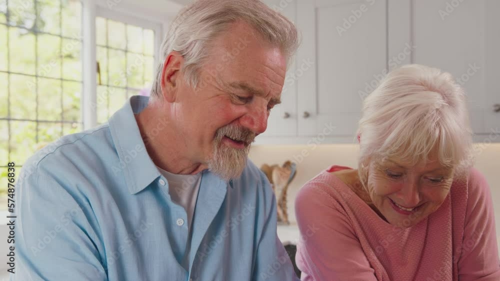 Smiling retired senior couple at home in kitchen signing legal or financial document together - shot in slow motion Smiling retired senior couple at home in kitchen signing legal or financial document together - shot in slow motion