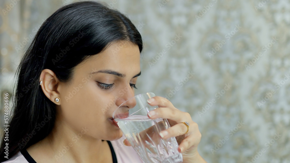 Closeup shot of an attractive young girl drinking from a glassful of freshwater. A beautiful Indian female having a glass of cold water against a blurred background - healthy lifestyle concept Closeup shot of an attractive young girl drinking from a glassful of freshwater. A beautiful Indian female having a glass of cold water against a blurred background - healthy lifestyle concept