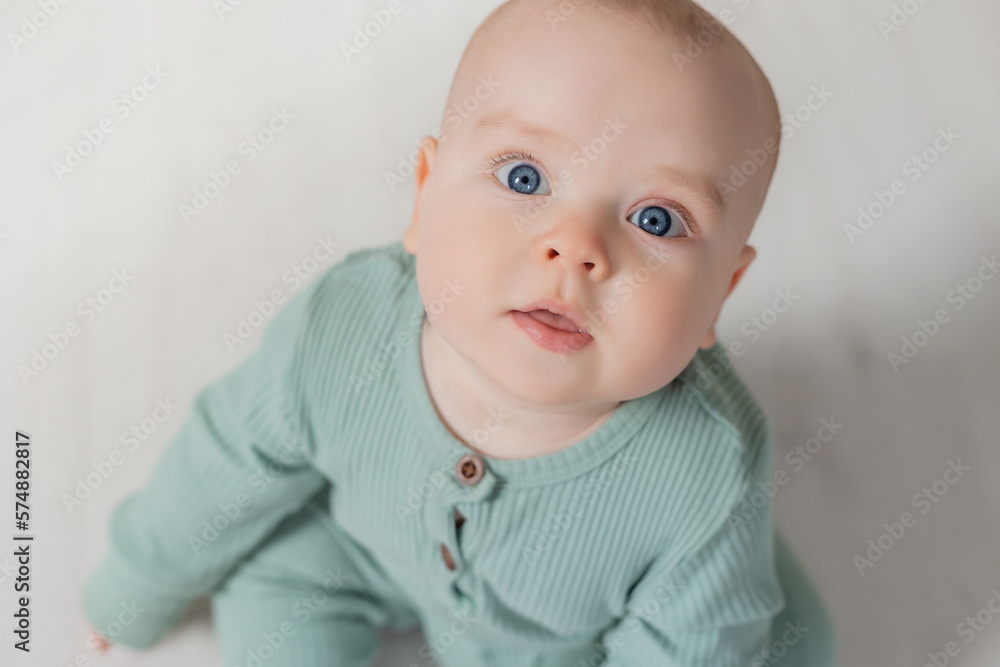 portrait of a charming chubby baby in a green jumpsuit sitting on the floor. top view portrait of a charming chubby baby in a green jumpsuit sitting on the floor. top view