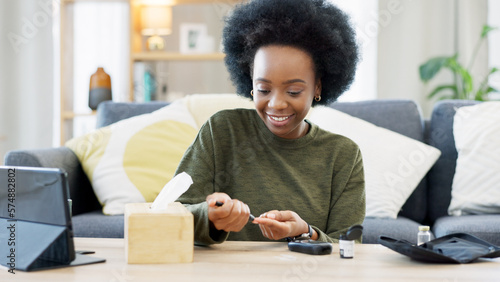 Happy African American woman using a glucose monitoring device at home. Smiling black female checking her sugar level with a rapid test result kit, daily routine of diabetic care in a living room photo