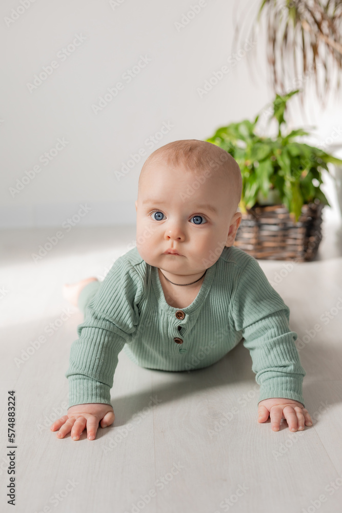 cute chubby-cheeked baby in a green jumpsuit is lying on the floor next to a houseplant cute chubby-cheeked baby in a green jumpsuit is lying on the floor next to a houseplant