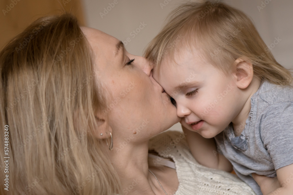 Blond mother kissing little daughter close up indoor portrait Blond mother kissing little daughter close up indoor portrait