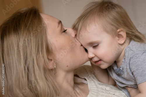 Blond mother kissing little daughter close up indoor portrait