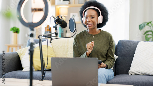 Cool afro journalist using digital tablet, talking into microphone and hosting podcast or broadcasting news while wearing headphones. Excited young woman using technology to promote on air from home photo