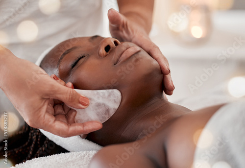 Black woman, gua sha massage and luxury face treatment of a young female with spa facial. Skincare, rose quartz tool and beauty in wellness clinic with client feeling calm and zen from dermatology photo