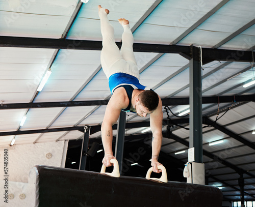 Man, acrobat and gymnastics upside down in balance for fitness practice, training or workout at gym. Professional male gymnast holding up body weight in pommel horse, athletics or strength exercise