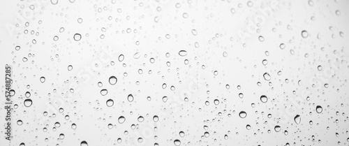 Minimal grayscale backdrop with rain droplets on white glass. Light wet window with rainy drops closeup in black-white. Blurry minimalist monochrome background of window glass with raindrops close up.