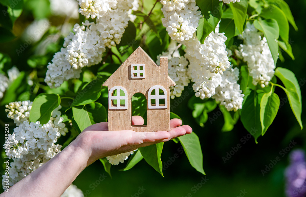 The girl holds the house symbol against the background of blossoming white lilac
The girl holds the house symbol against the background of blossoming white lilac