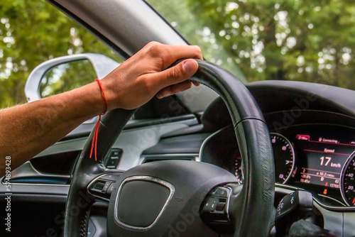 A man's hand with a red thread holds a black steering wheel